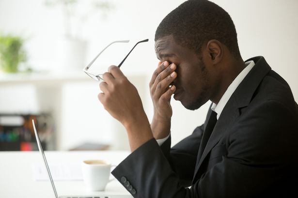 パソコンに疲れたアフリカのビジネスマンがメガネを外すと、目が疲れる。